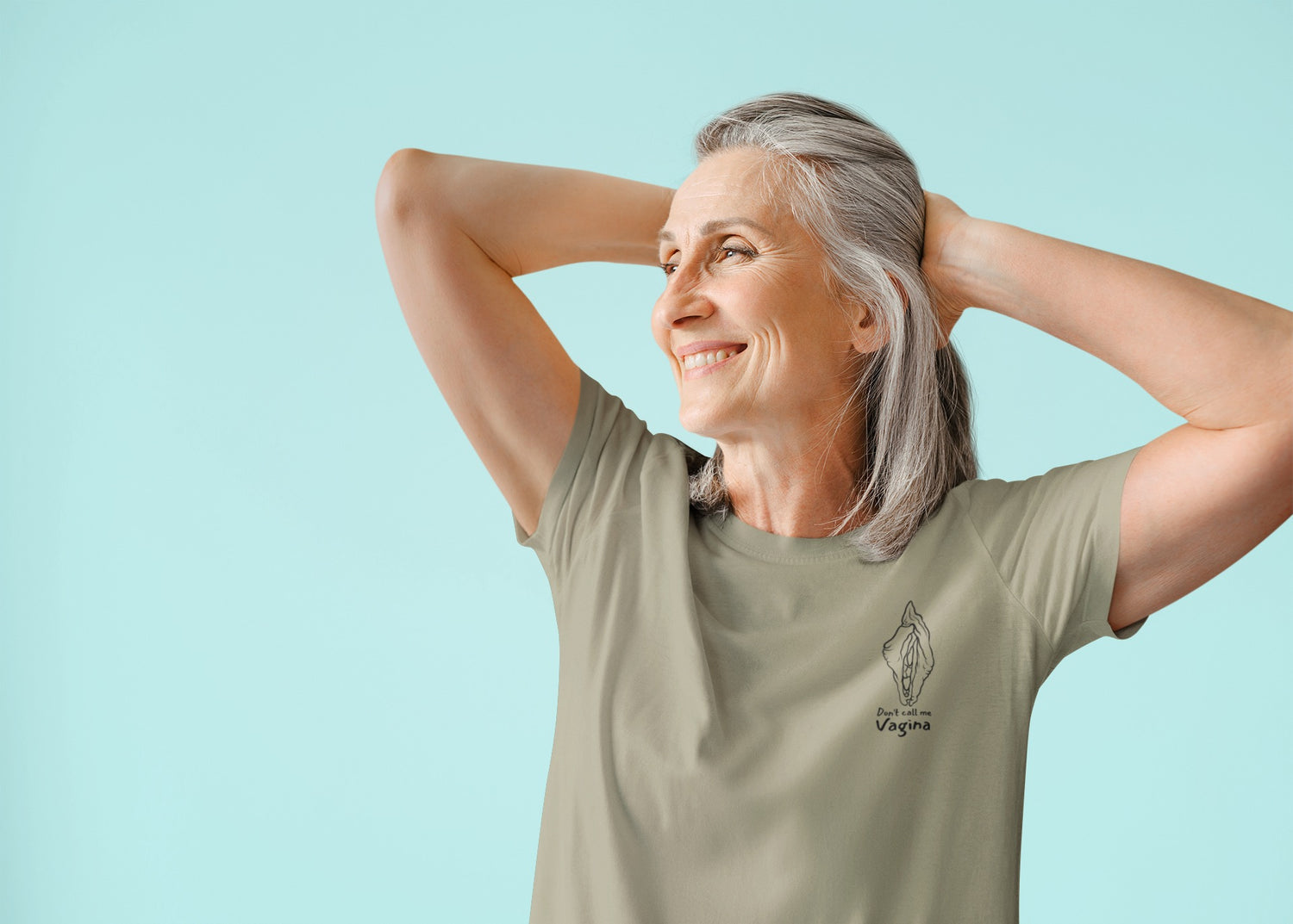 A photo of a person wearing the "Don't Call Me Vagina" t-shirt while pulling back their long hair and smiling with their elbows up, gazing into the distance.